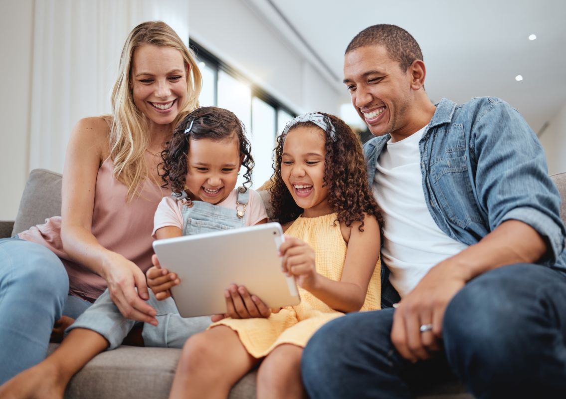 Photo shows a family enjoying a game or video on a digital device.